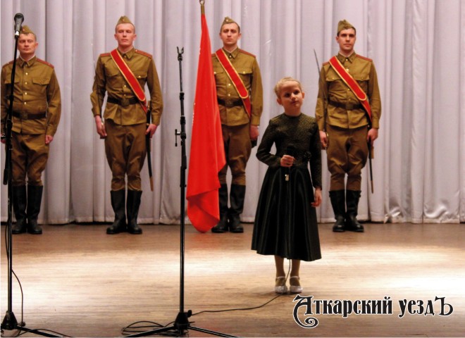 Маленькая девочка поет песню о Великой Отечественной войне на фоне Знамени Победы